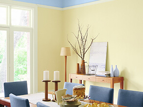 Colourful yellow and blue dining room with timber table and bench with plush blue chairs and candle